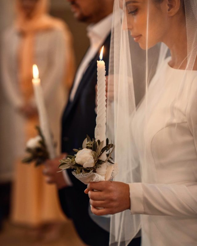 Регина Бурд и Сергей Жуков держат свечу в церкви во время венчания