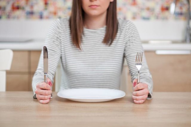 девушка сидит за столом с ножом и вилкой
