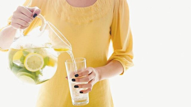 девушка наливает в стакан воду с лимоном